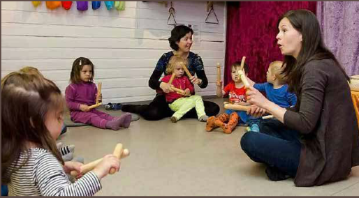 Barn og voksne sitter i en ring og spiller på instrumenter. Foto