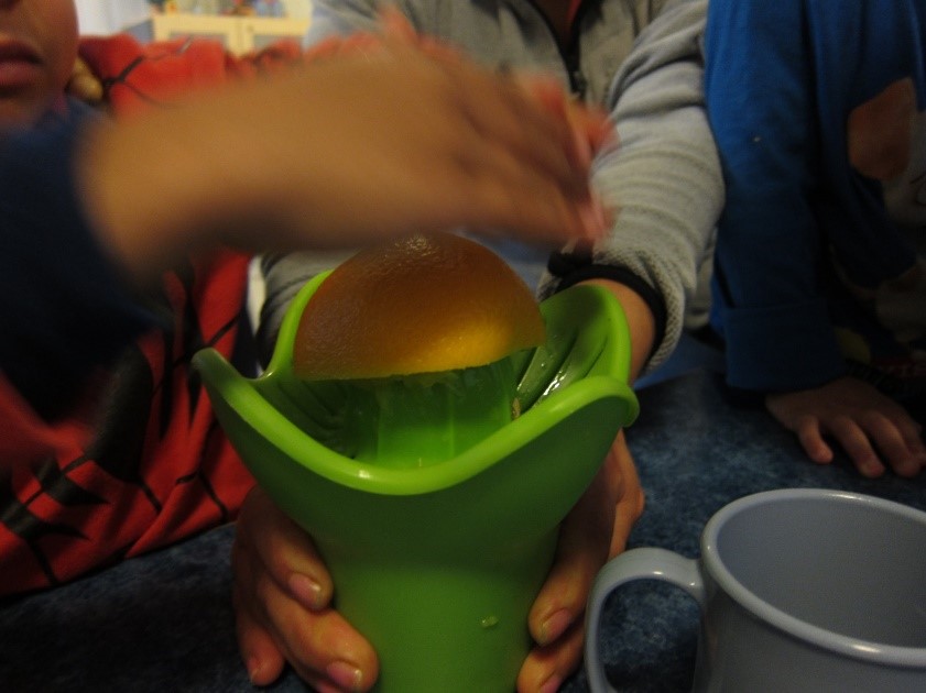 barnehender presser en appelsin i en appelsinpresse