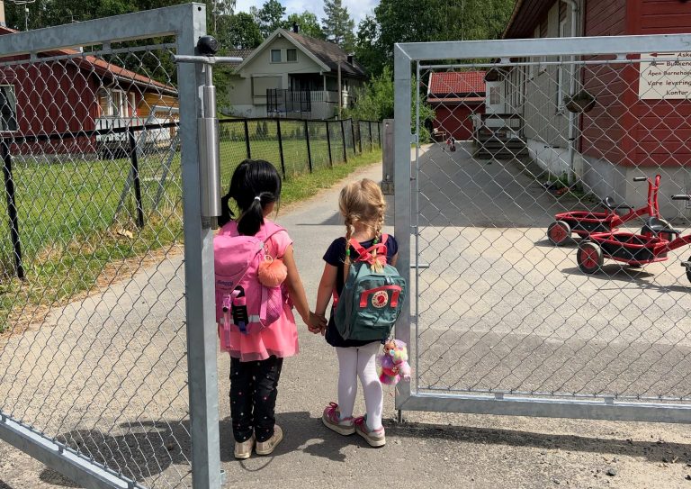 to barn går hånd i hånd inn porten til en barnehage