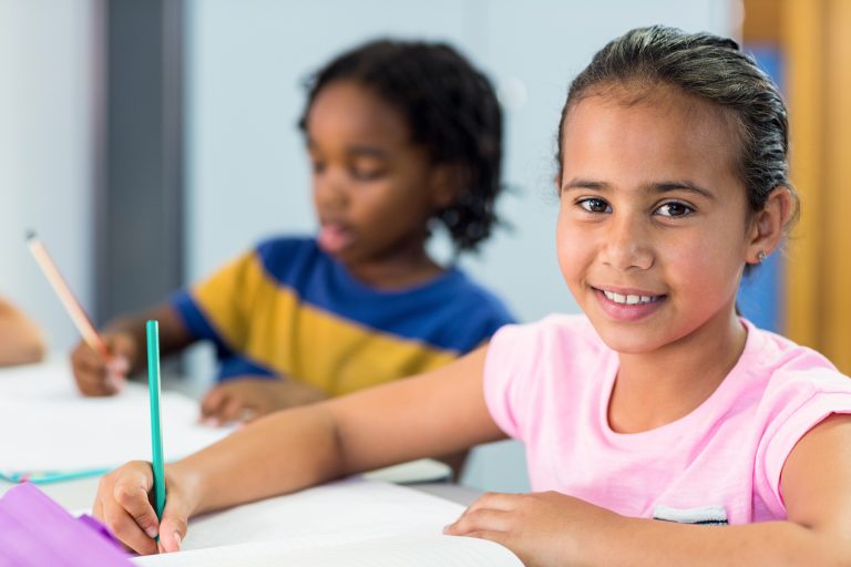 En smilende jente sitter og skriver i klasserommet