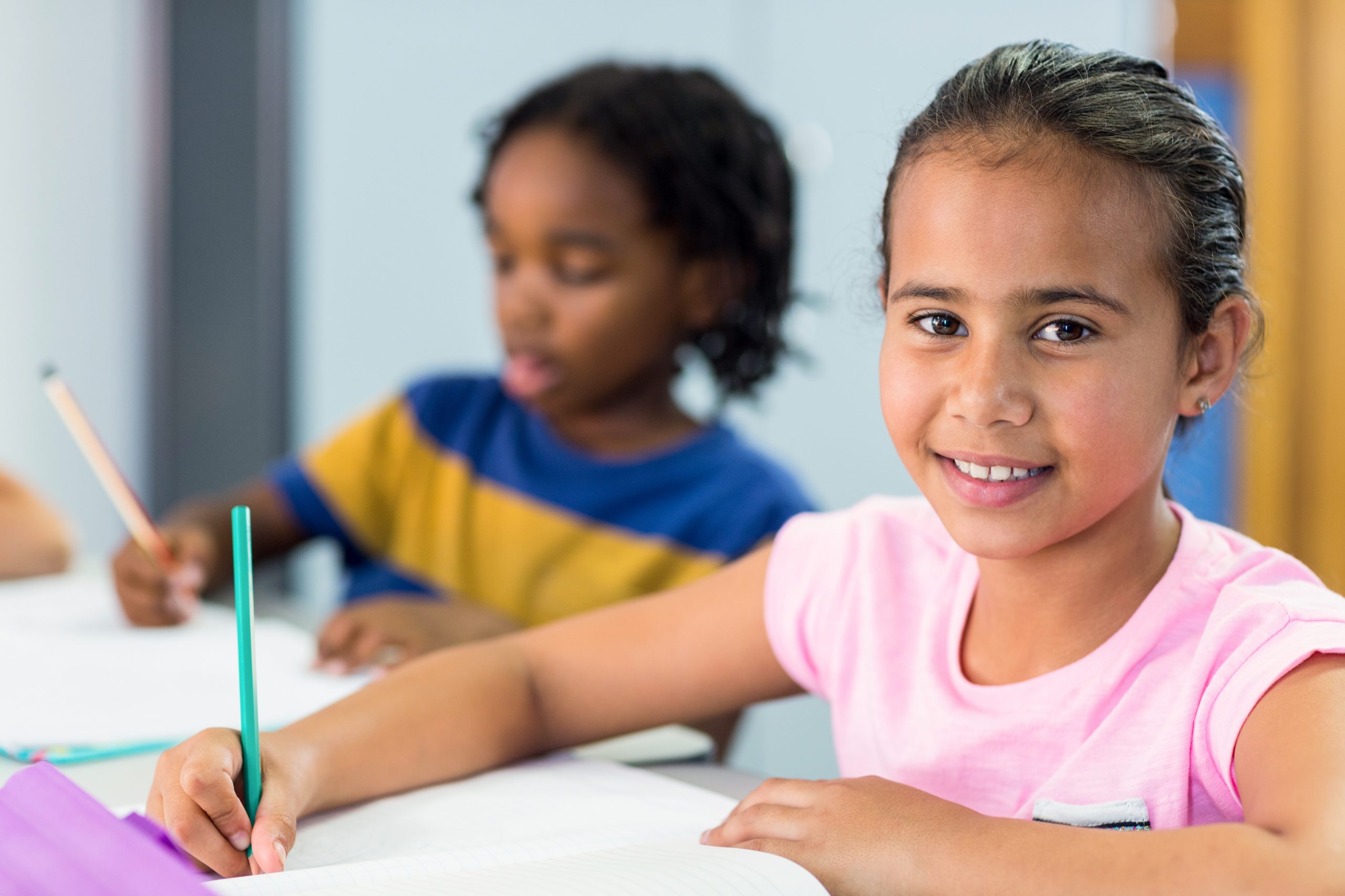 En smilende jente sitter og skriver i klasserommet
