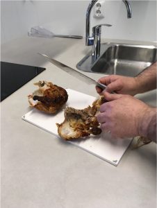 Foto av to hender som skjærer opp en kylling på en fjøl.