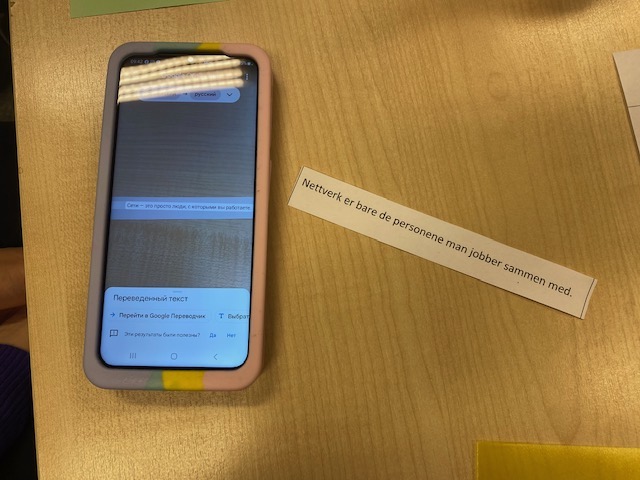 Fot av en setning på et stykke papir. ved siden av ligger en mobiltelefon med oversettelse til ukrainsk.