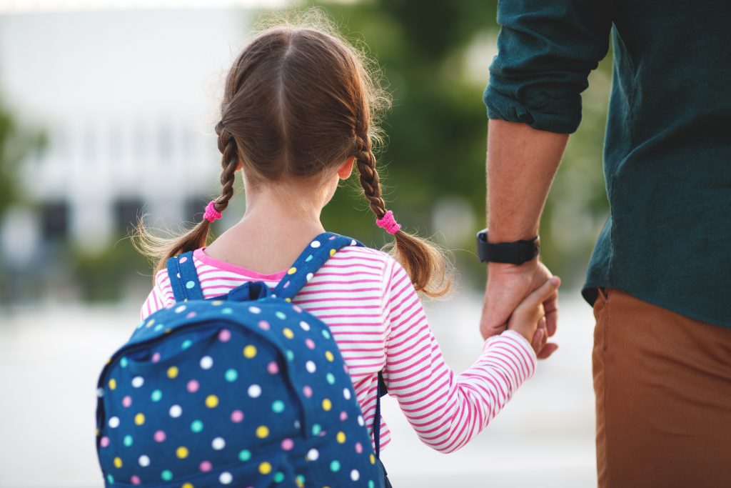 En jente holder pappaen sin i hånda på vei til skolen