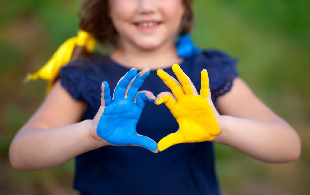 Foto av jente som holder opp hendene som et hjerte. Den ene hånden er malt blå og den andre er malt gul.