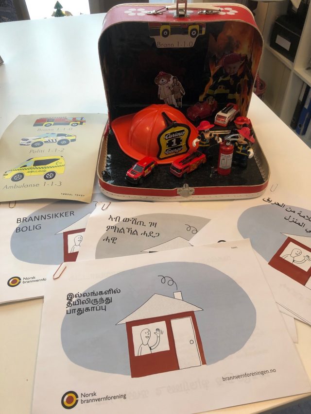 Bilde av koffert med gjenstander som illustrerer tema brann og brosjyrer med informasjon om brannvern på flere språ