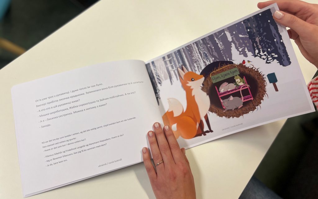 en oppslått bok med tekst på to språk til venstre og en illustasjon av en rev og dyr inne i en vott til høyre.