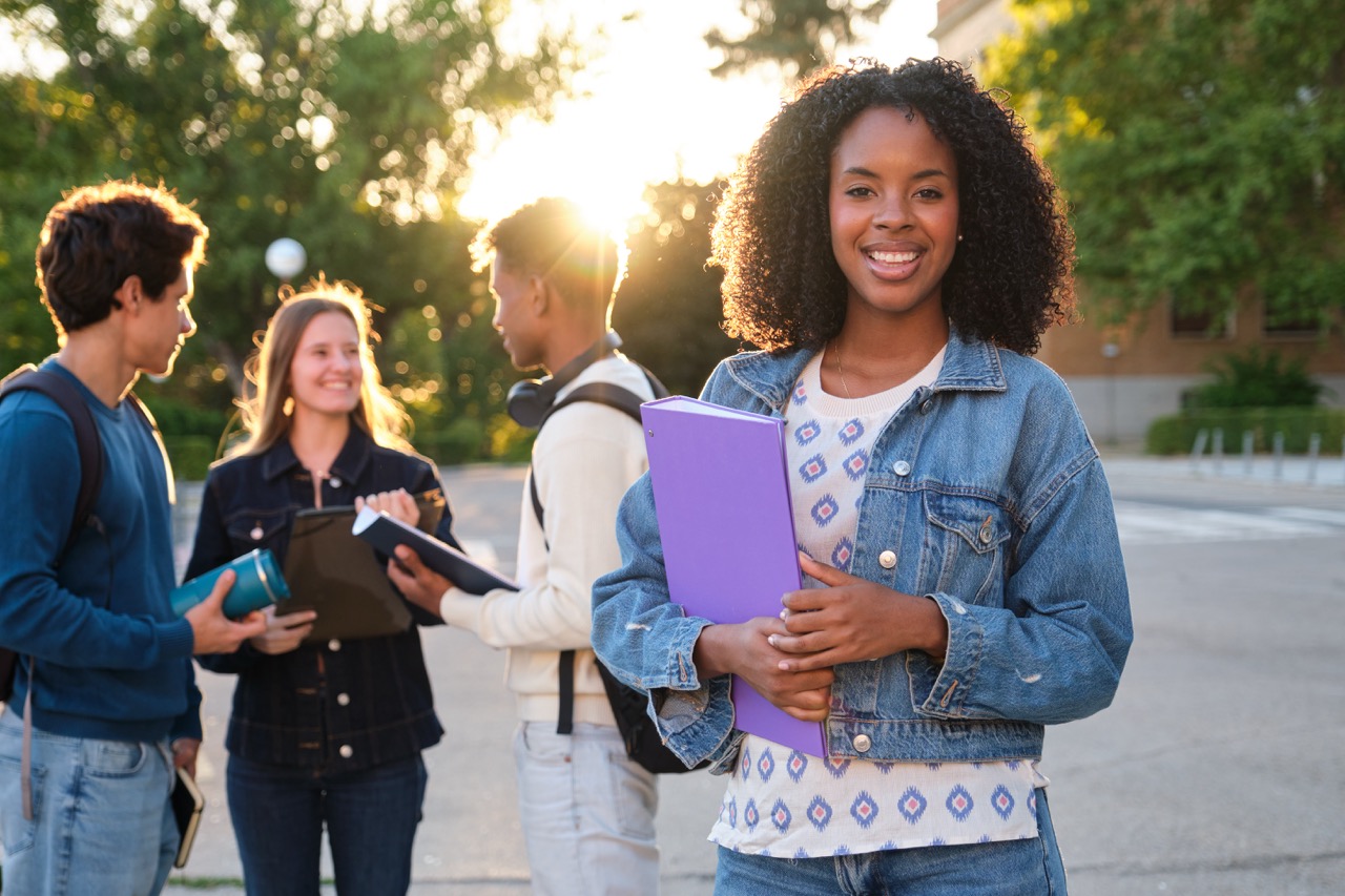 Foto av skoleungdom. En jente står foran de andre. Hun holder en skrivebok i armen.