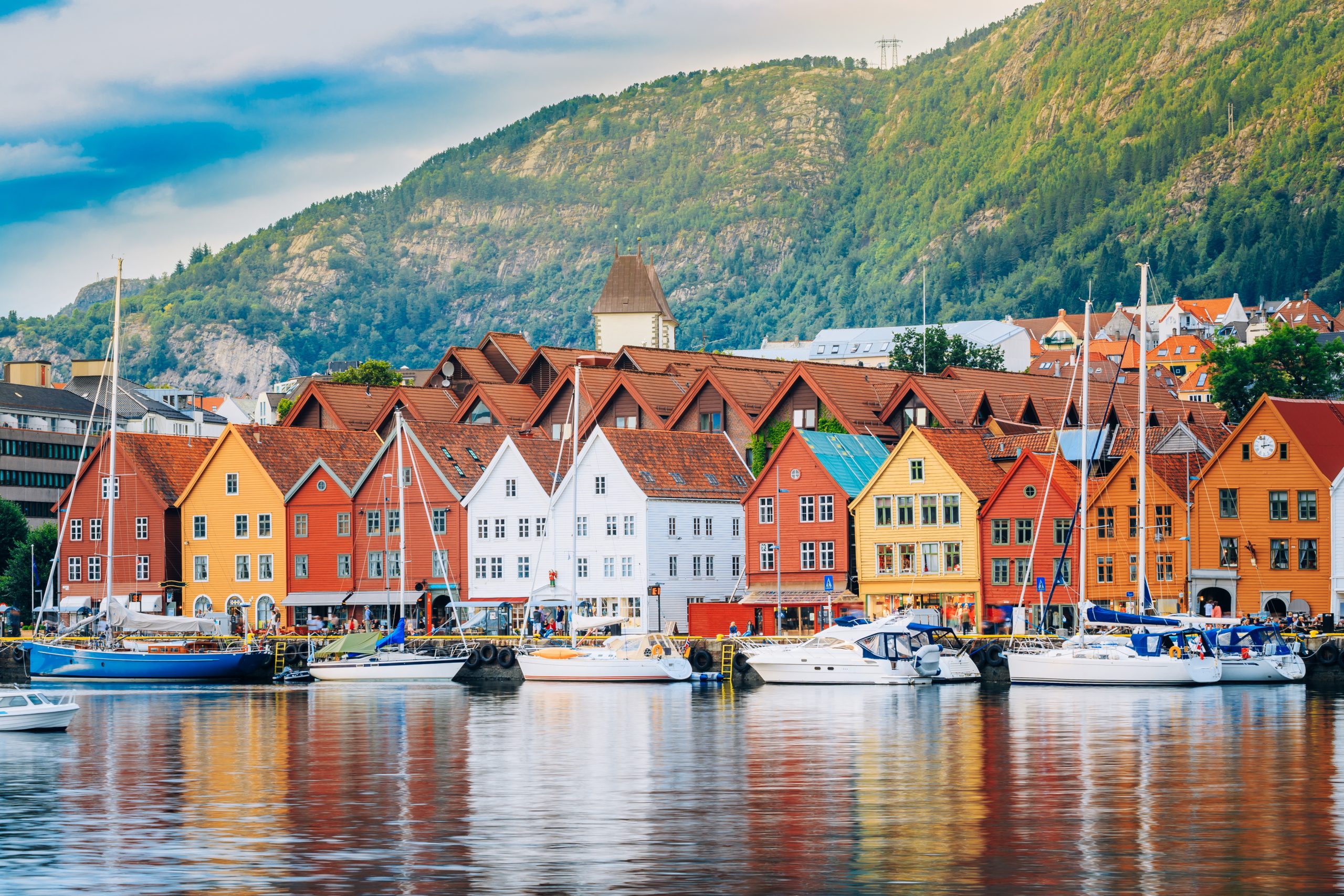 Fotografi av Bryggen i Bergen. Gamle trehus i ulike farger ligger ved en kai med seilbåter.
