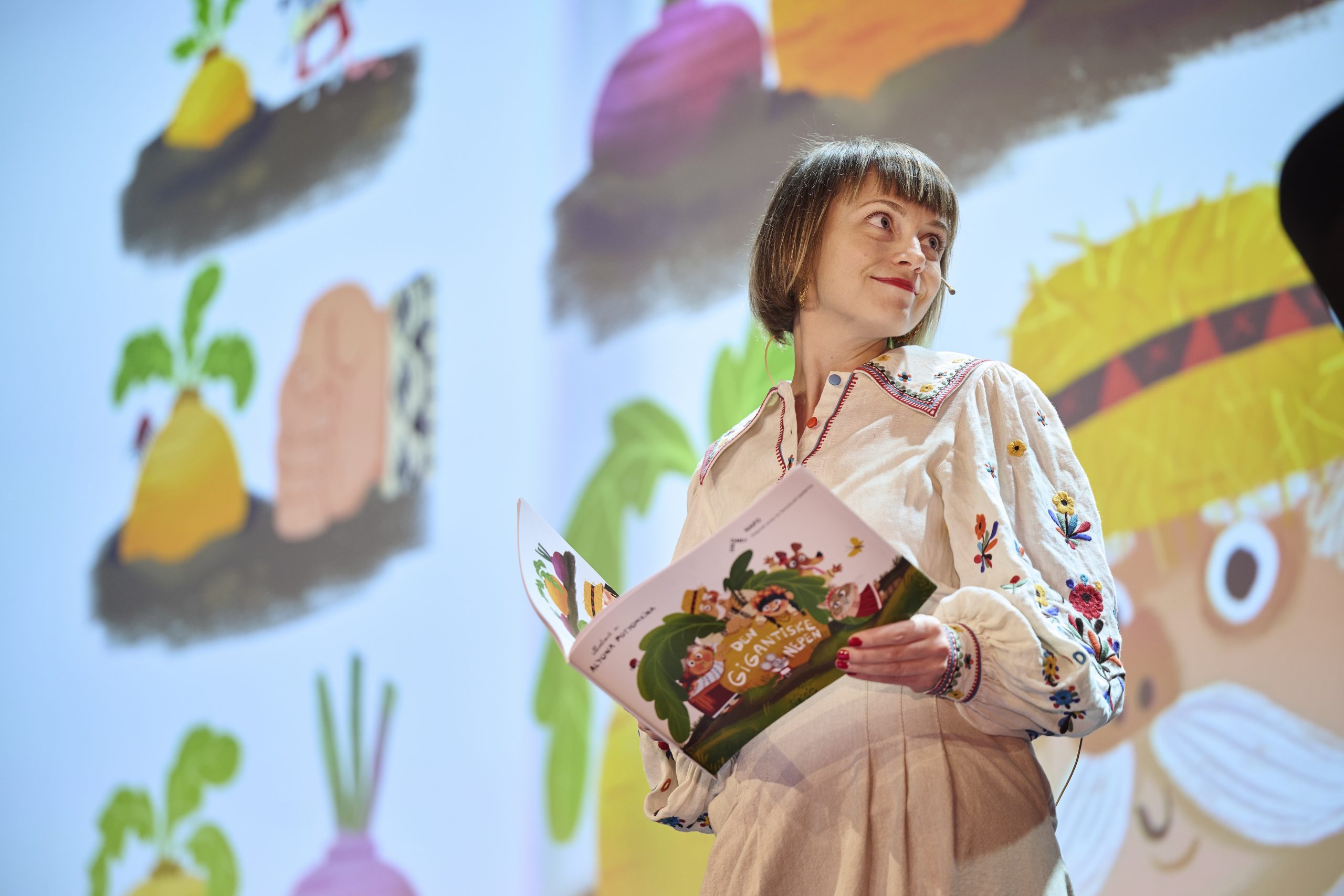 Foto av Svitlana Kucherenko som holder boka Den gigantiske nepen på en scene