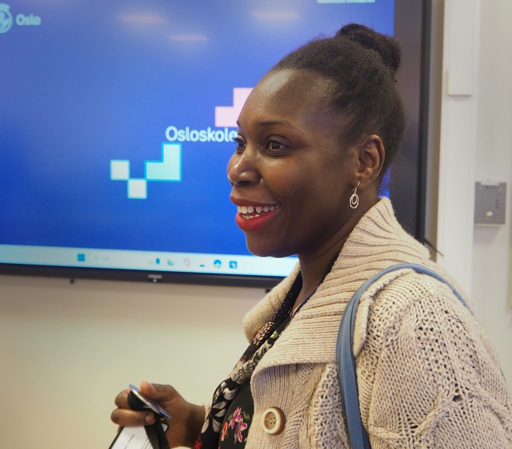 Foto av Fatou Ceesay i profil i klasserommet. Hun smiler bredt. I bakgrunnen er en stor touch-skjerm det står Osloskolen på.