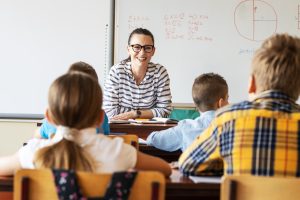 Foto av lærer som smiler foran elever i klasserommet.