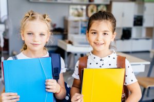 Foto av to skoleelver som holder en blå og en gul mappe i et klasserom