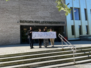 Foto av fire deltakere fra klassen som vant Verdens kuleste ord på trappa foran Bergen inkluderingssenter. I henda holder de en stor plakat hvor det står gohirahira