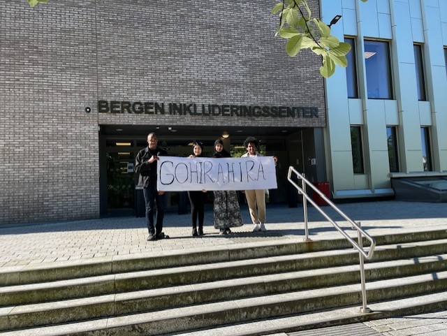 Foto av fire deltakere fra klassen som vant Verdens kuleste ord på trappa foran Bergen inkluderingssenter. I henda holder de en stor plakat hvor det står gohirahira