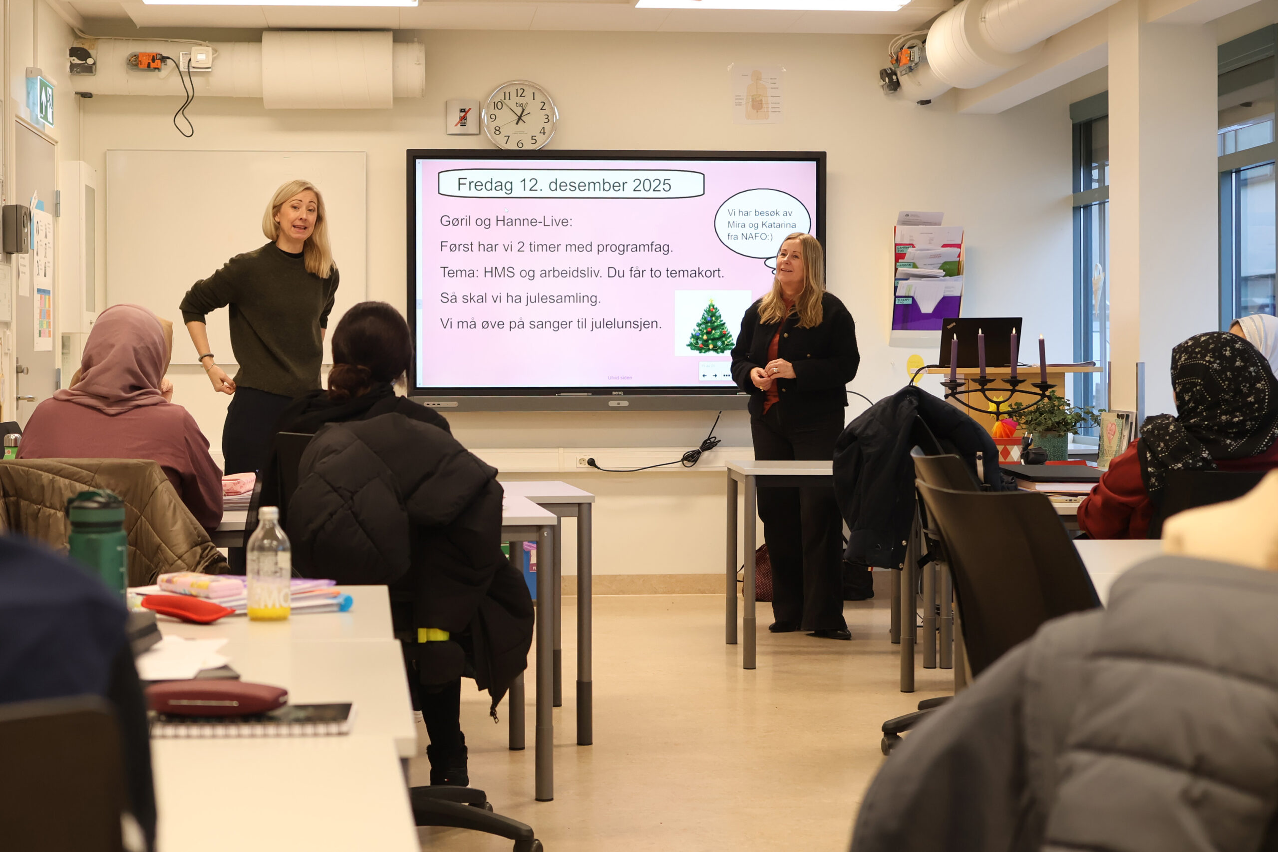 Foto fra et klasserom i voksenopplæringen. Lærerne Hanne Live og Gøril står ved en smart board og underviser en klasse. Noen deltakere sitter ved arbeidsbord og ser mot lærerne. Foto: Katarina Hundal